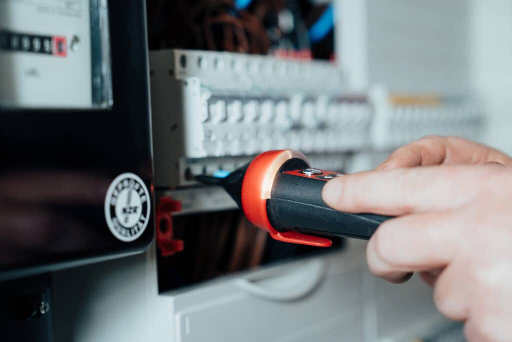 Ein Mitarbeiter eines IT-Unternehmens in Dresden prüft mit einem digitalen Spannungsprüfer die elektrischen Leitungen in einer Schalttafel auf Sicherheit und Funktionalität.