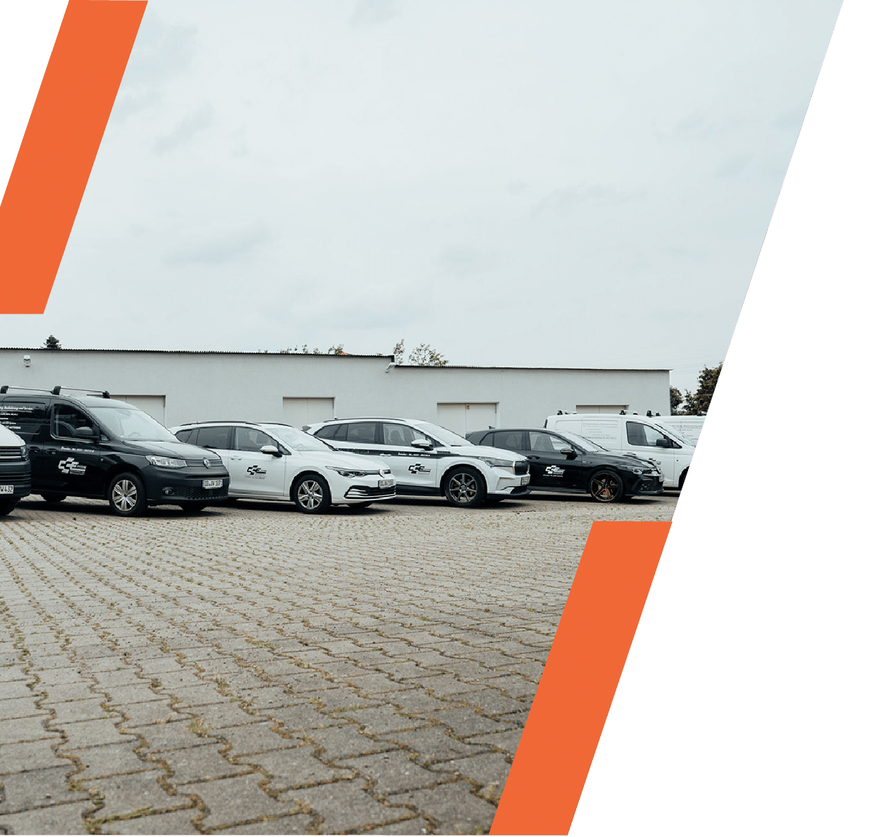 Eine Reihe weißer und schwarzer Firmenfahrzeuge parkt auf einem gepflasterten Parkplatz vor einem schlichten weißen Gebäude, eingerahmt von zwei kräftigen orangefarbenen Diagonalstreifen - ein perfektes Bild für die Professionalität eines auf Netzwerktechnik spezialisierten IT-Dienstleisters in Dresden.