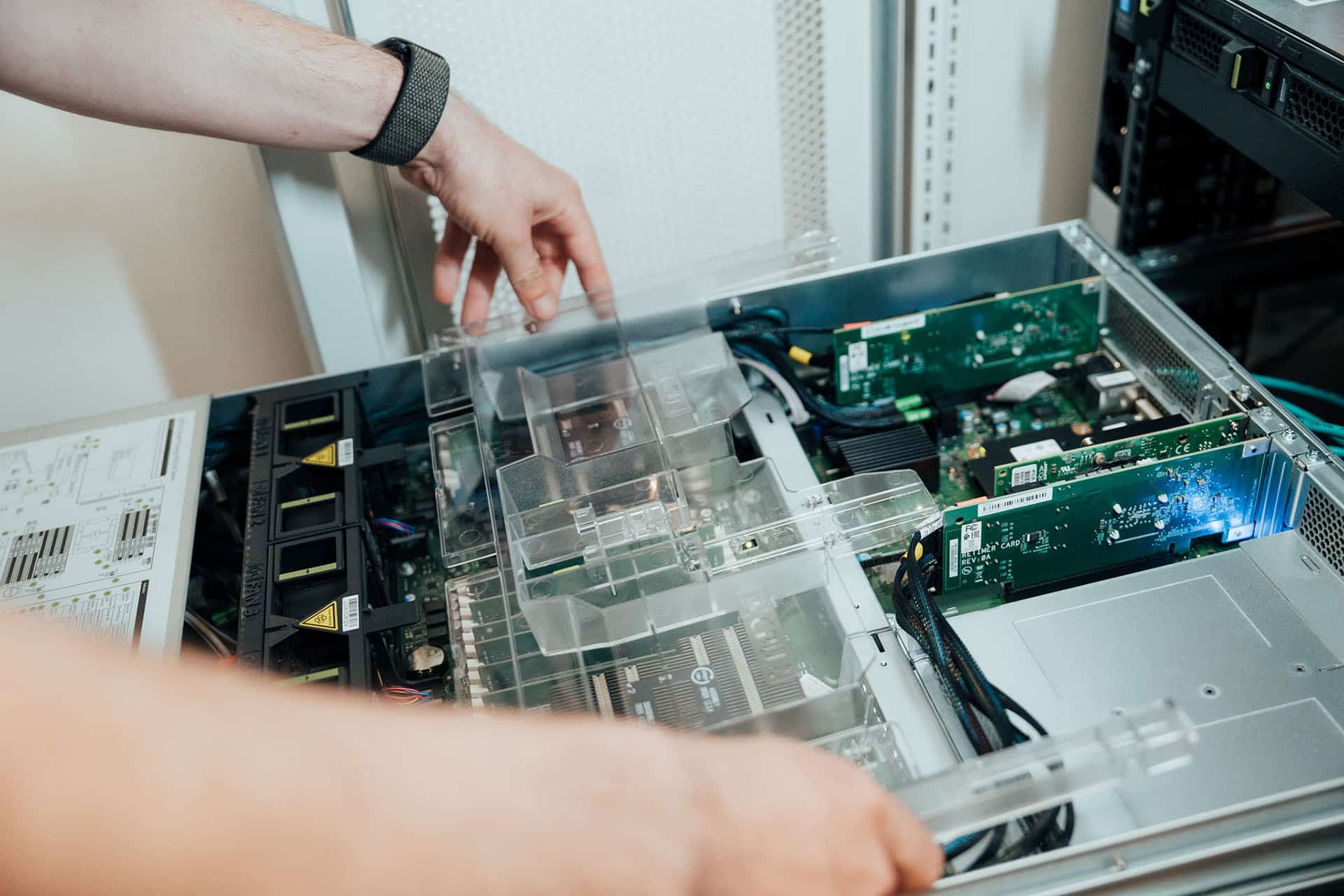 Die Hände einer Person arbeiten im Inneren eines offenen Computerservers und justieren oder installieren interne Komponenten und Leiterplatten innerhalb eines Metallgehäuses als Teil der Wartung der Serverinfrastruktur.